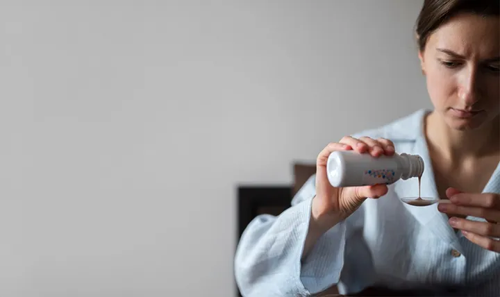 A person pouring liquid from a bottle into a measuring cap.